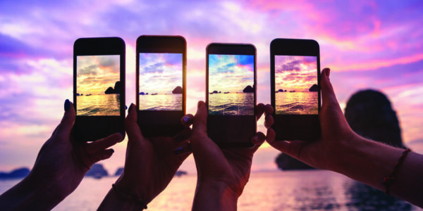 Closeup photo of four hands with mobile phones taking photo of beautiful sunset over sea bay